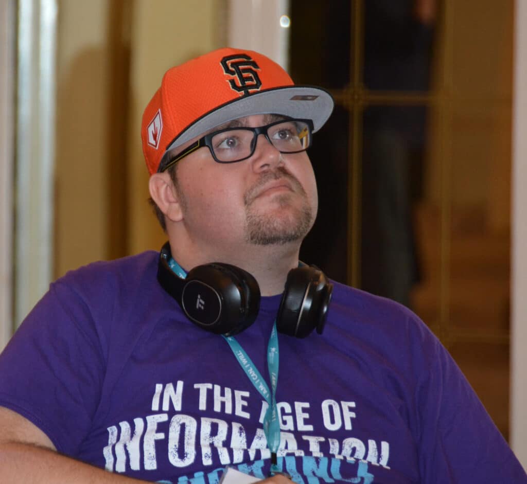 Mitchell B. Young man with hat, glasses, and headphones intently watches MS program.