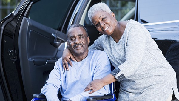 Man in wheelchair with woman next to him in front of car