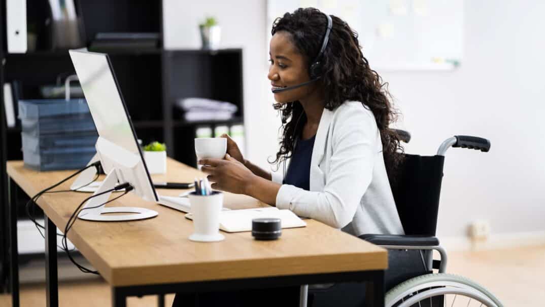 Young woman in a wheelchair sitting at a computer desk at work