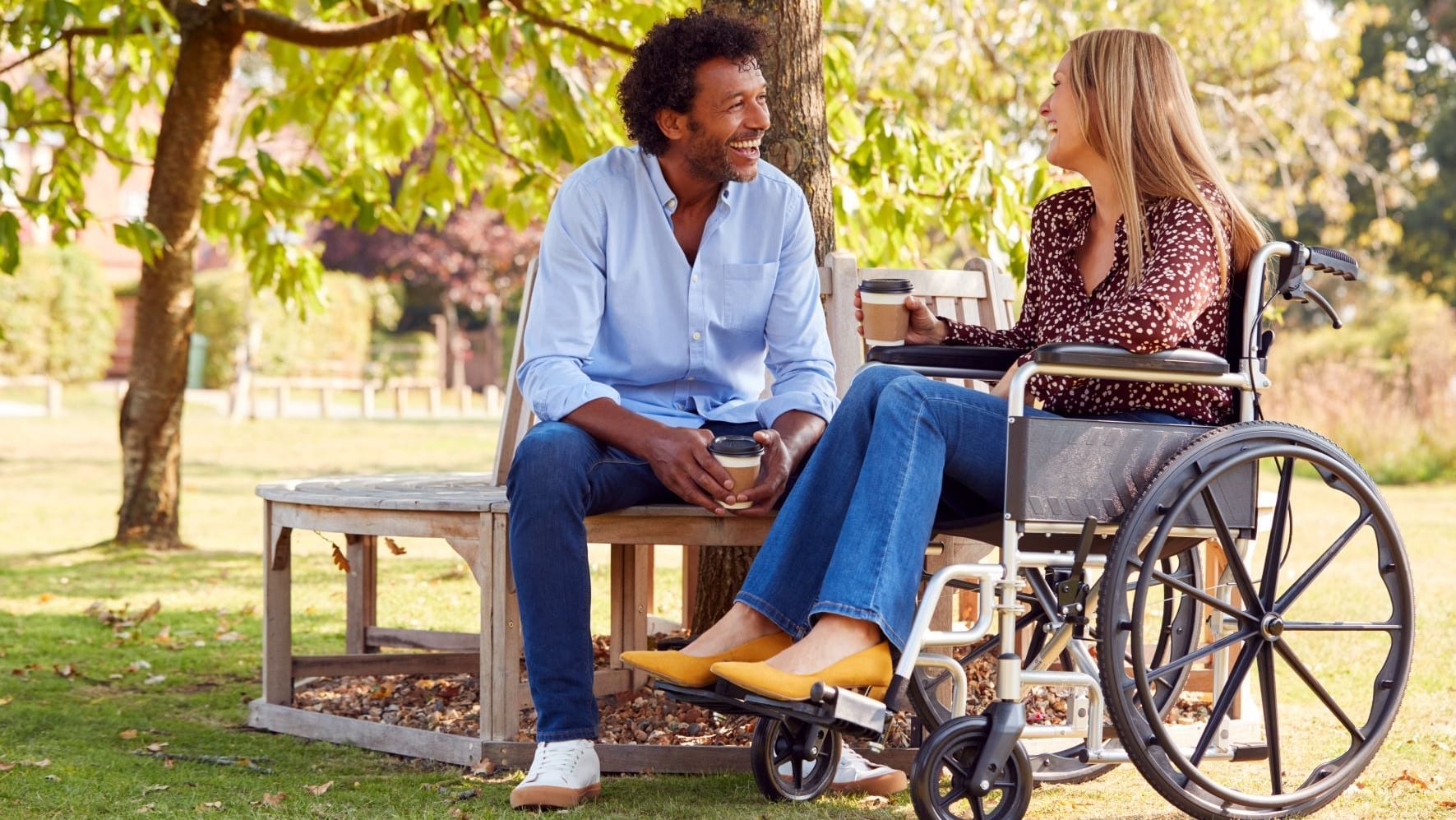 Woman in a wheelchair drinking coffee outside with her male friend