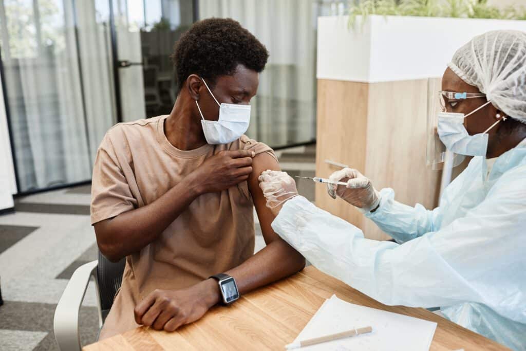 Young Black Man Sitting At Doctors Office And Getting A Vaccine