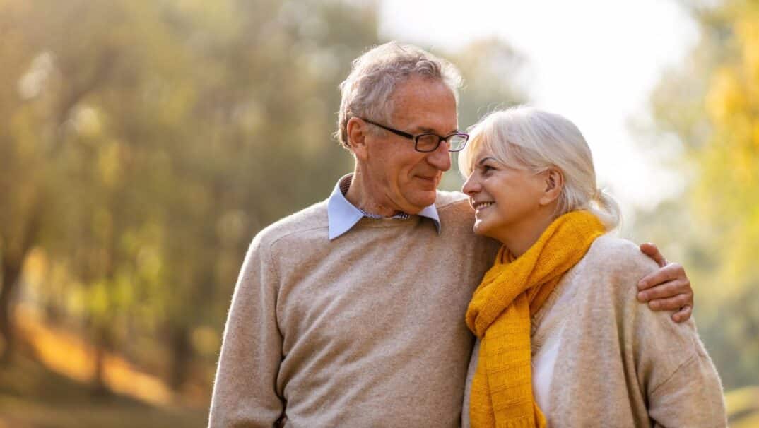 Older couple walking outside with their arms around one another.