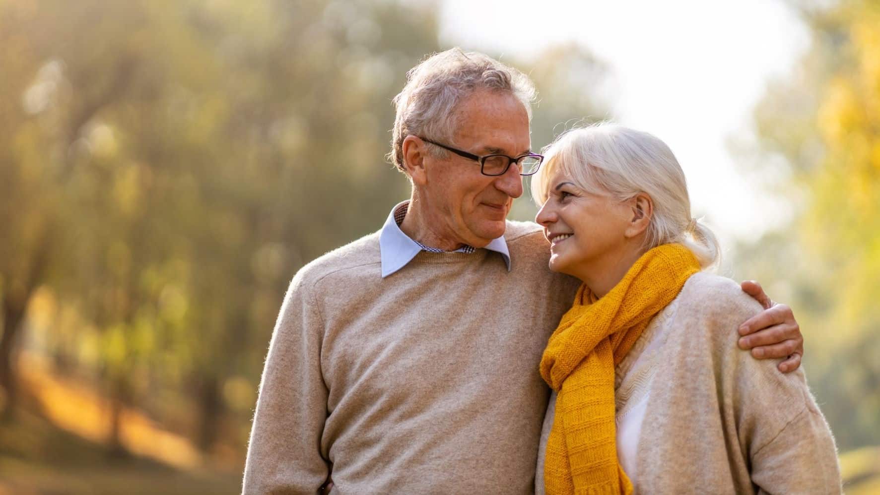Older couple walking outside with their arms around one another.