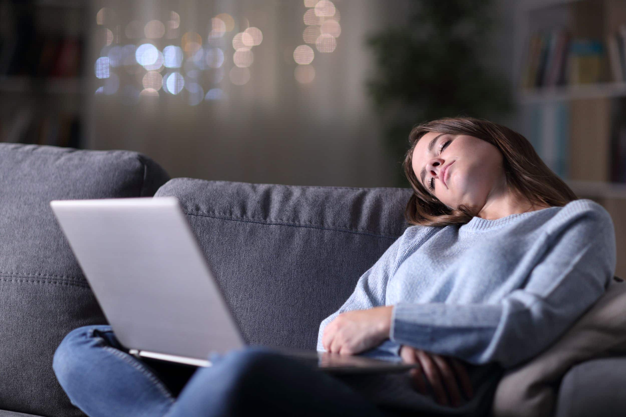 Young woman asleep sitting up with laptop on her lap