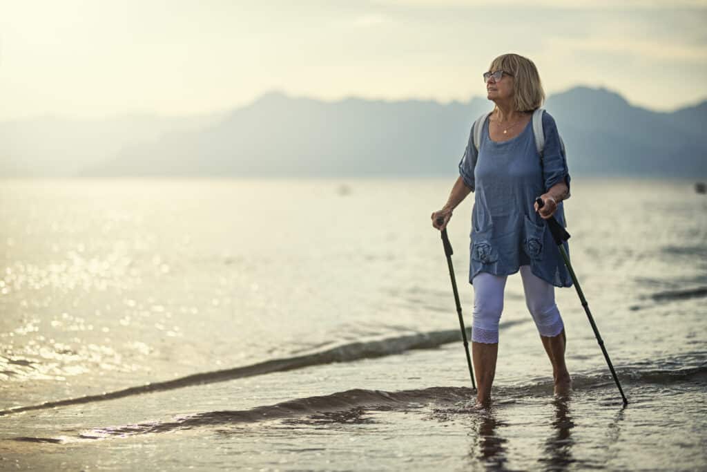 Woman walking on the beach with walking sticks
