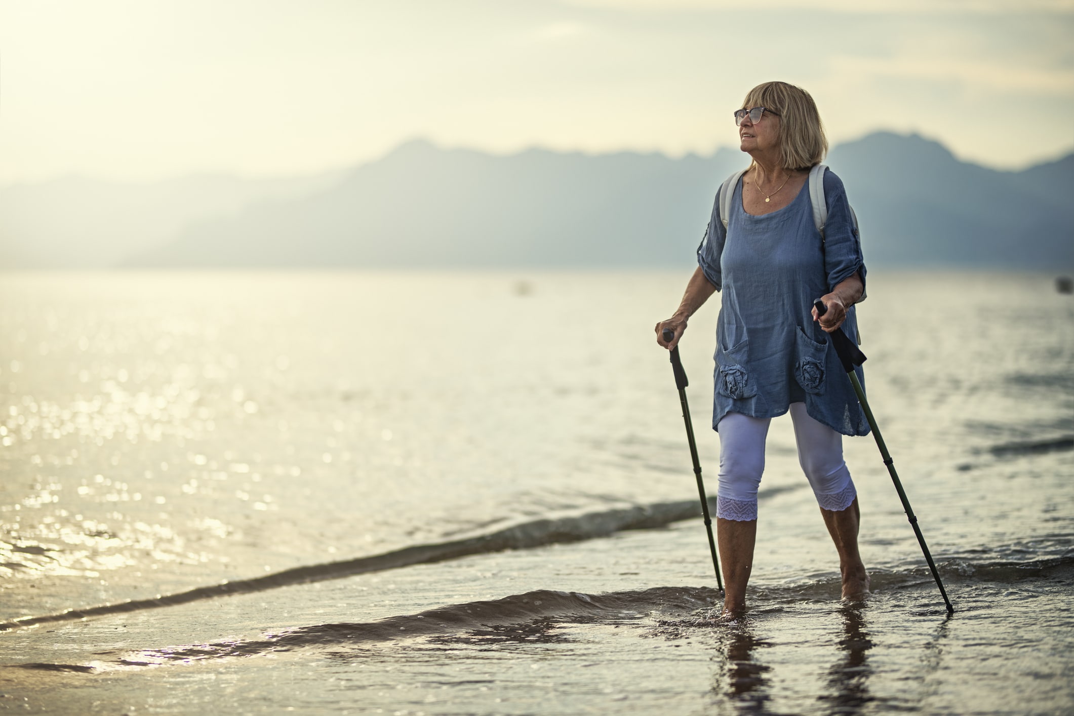 Woman walking on the beach with walking sticks