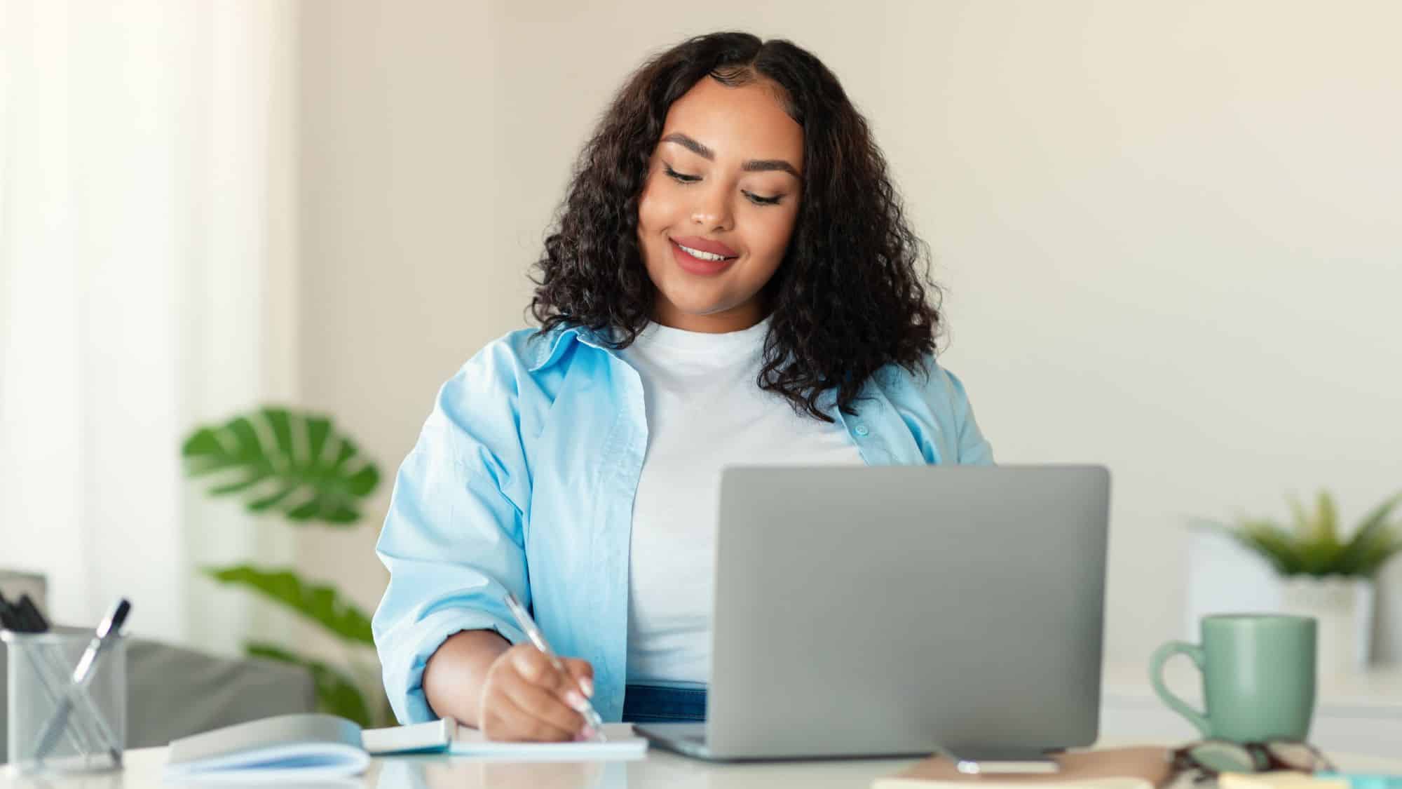Young adult at a laptop writing notes