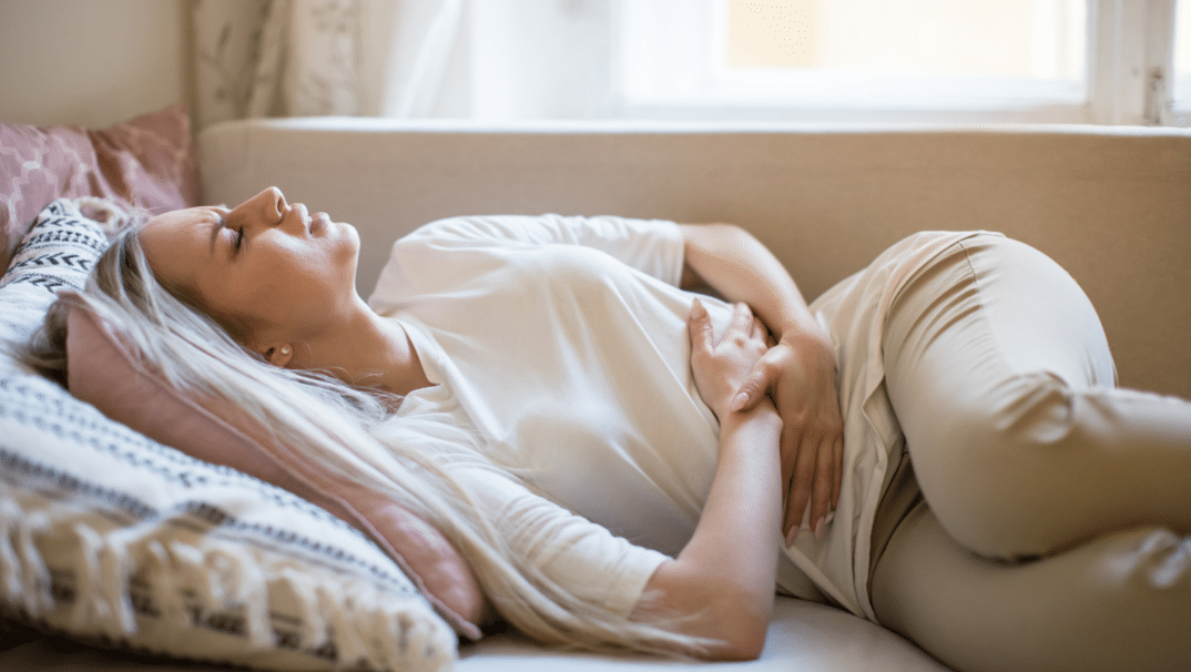 Woman holding abdomen while laying down on her bed.