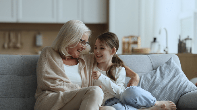 Older woman cuddling with her young granddaughter on a couch.