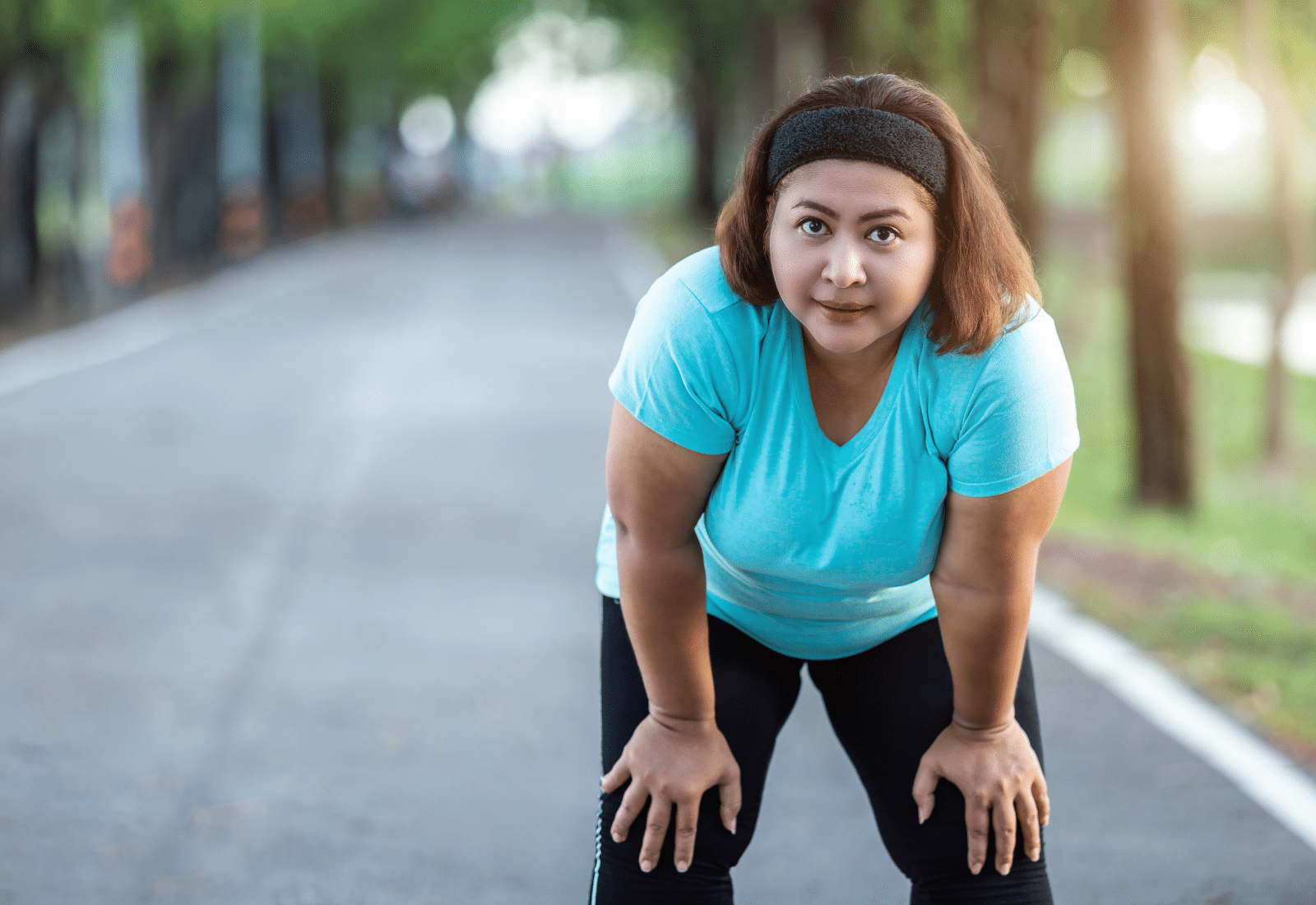 middle aged woman leans with her hands on her knees, looking tired but proud from exercise